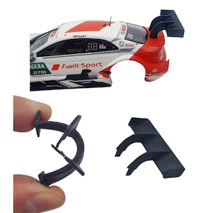 Könnte beinhalten: Ein schwarzer Spoiler aus Kunststoff für ein Modellauto. Der Spoiler hat drei Finnen und ist so konzipiert, dass er die Aerodynamik verbessert. Der Spoiler wird in zwei verschiedenen Positionen gezeigt, einmal mit ausgefahrenen Finnen und einmal mit eingeklappten Finnen.