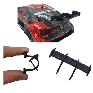 Könnte beinhalten: Ein schwarzer Spoiler aus Kunststoff mit drei verstellbaren Finnen. Der Spoiler ist für ein Modellauto konzipiert und wird in einer Nahaufnahme gezeigt.