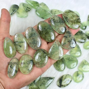 May include: A collection of green and black gemstone cabochons in a variety of shapes and sizes. The stones are translucent with black inclusions.