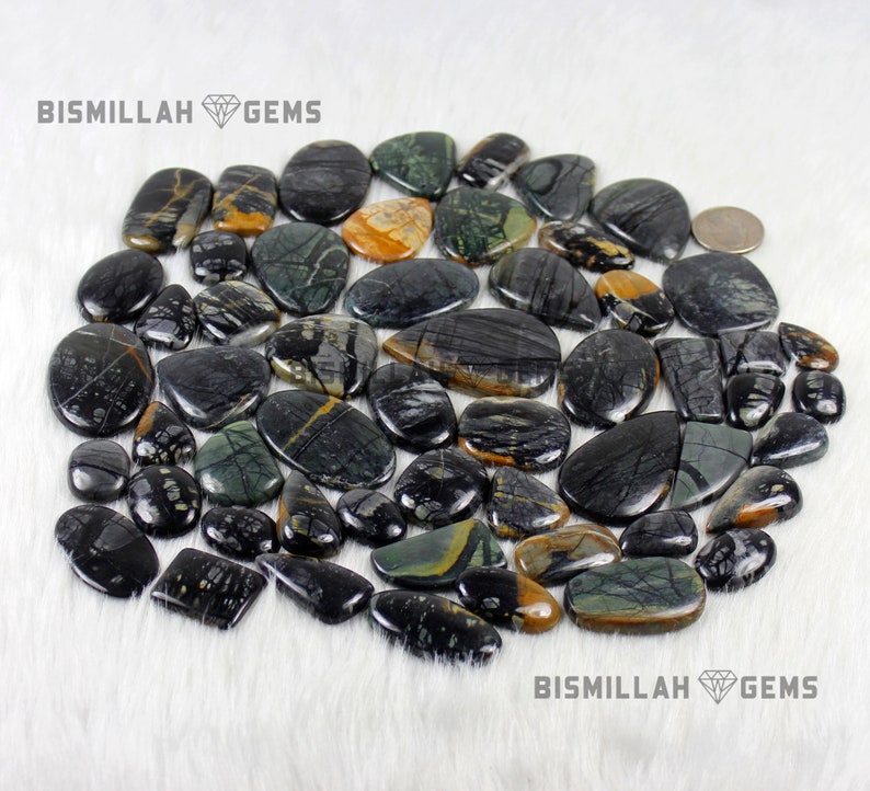 May include: A collection of black, green, and yellow gemstone cabochons. The stones are smooth and polished, with a variety of patterns and textures. BISMILLAH GEMS is printed on the image.