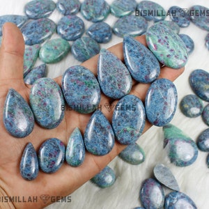 May include: A collection of blue and green gemstone cabochons in a teardrop shape. The stones have a speckled pattern with red and white inclusions. The stones are displayed on a hand.