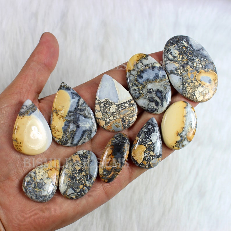 K&ouml;nnte beinhalten: Eine Sammlung von zehn tropfenf&ouml;rmigen, polierten, nat&uuml;rlichen Stein-Cabochons. Die Steine sind eine Mischung aus Creme, Braun und Grau mit einem marmorierten Muster.