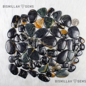 May include: A collection of 35 black, green, and yellow gemstone cabochons. The stones are all different shapes and sizes, and they have a variety of patterns. BISMILLAH GEMS is printed on the image.