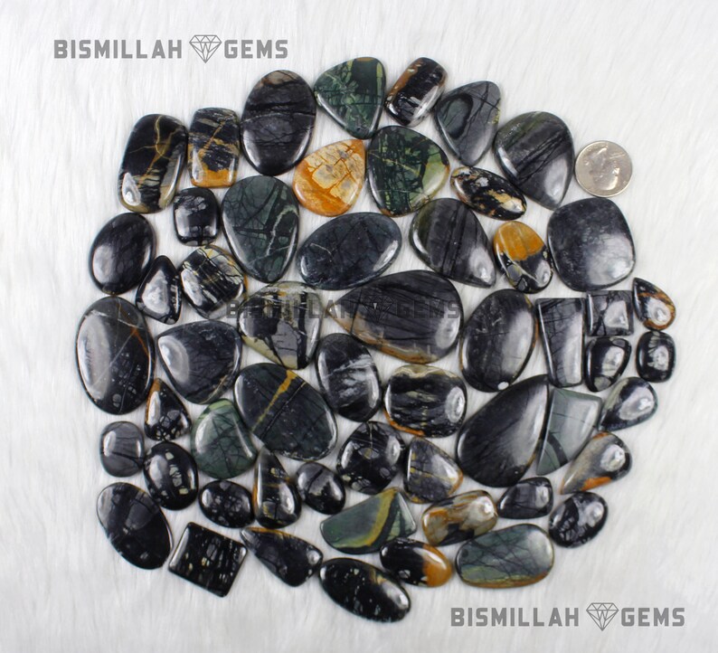 May include: A collection of 35 black, green, and yellow gemstone cabochons. The stones are all different shapes and sizes, and they have a variety of patterns. BISMILLAH GEMS is printed on the image.