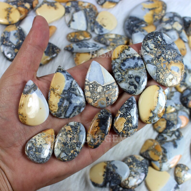 K&ouml;nnte beinhalten: Eine Sammlung von 12 tropfenf&ouml;rmigen, polierten, nat&uuml;rlichen Edelstein-Cabochons. Die Steine sind eine Mischung aus Braun, Beige, Grau und Wei&szlig; mit einem gesprenkelten Muster.