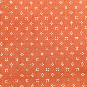 Könnte beinhalten: Nahaufnahme eines Stoffes mit einem sich wiederholenden Muster aus weißen vierzackigen Sternen auf orangefarbenem Hintergrund. Der Stoff hat ein strukturiertes Aussehen, was darauf hindeutet, dass er aus Baumwolle oder Leinen sein könnte. Das Muster ist gleichmäßig verteilt.