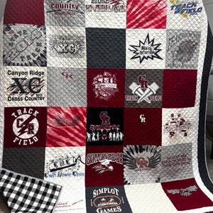 May include: A handmade quilt with maroon, grey, and white squares. The squares feature sports team logos and text, such as "Canyon Ridge" and "Track & Field." The quilt has a black and white checked backing and a quilted border. The quilt measures approximately 150cm x 180cm.