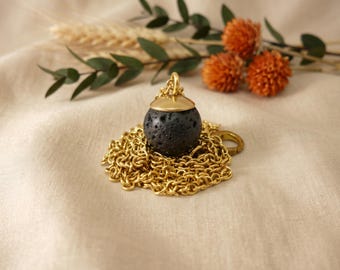 May include: A spherical black lava stone pendant with a smooth gold-toned metal cap, attached to a delicate gold-toned chain necklace. The porous, dark volcanic rock contrasts with the polished metallic finish of the cap and chain.