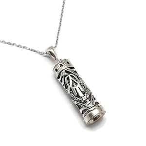 以下が含まれることがあります： 複雑な模様と装飾的なキャップが付いた、銀色のペンダントネックレス。ペンダントは繊細なチェーンから吊り下げられており、スタイリッシュなアクセサリーになっています。デザインには、詳細な透かし模様が含まれています。