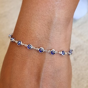 May include: A silver bracelet with a chain of blue and white evil eye charms.