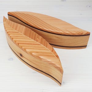 Peut inclure: Deux bols en bois avec une finition en bois naturel et une bordure noire. Les bols sont en forme de feuilles et sont imbriqués l'un dans l'autre.