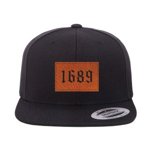 May include: Black baseball cap with a brown leather patch that says "1689" in black gothic font.