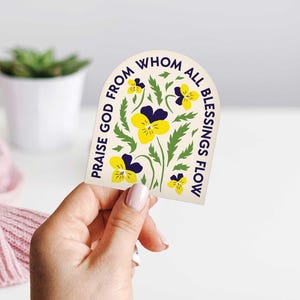 May include: A cream-colored sticker with a blue and yellow floral design. The text on the sticker reads "Praise God from whom all blessings flow."