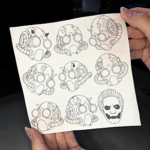 Könnte beinhalten: Ein Blatt Papier mit neun Schwarzweißzeichnungen von steampunk-artigen Gasmasken. Die Masken haben verschiedene Designs, darunter Hörner, Zahnräder und Rohre. Die letzte Zeichnung zeigt ein Gesicht mit einem unheilvollen Lächeln.