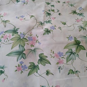 Peut inclure: Tissu blanc avec un motif floral répété. Le motif présente des feuilles de lierre vertes, de petites fleurs roses et bleues et des vignes sinueuses. L'esthétique générale est douce et botanique.