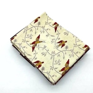 Può includere: Tessuto piegato con sfondo crema con un motivo ripetuto di uccelli in volo, con colori rosso e oro. Gli uccelli sono circondati da un delicato design di vite e foglie in nero. Il tessuto è piegato e impilato.