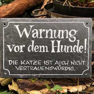 Op de afbeelding: Een zwart leisteen bord met witte letters met de tekst "Waarschuwing voor de hond! De kat is ook niet betrouwbaar."