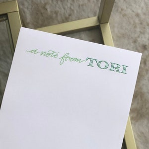 Może przedstawiać: Biały notatnik z zielonym napisem "a note from TORI". Notatnik leży na złotym metalowym i szklanym stole.