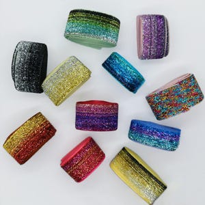 Puede incluir: Surtido de cintas elásticas brillantes de colores. La cinta está disponible en una variedad de colores, incluyendo negro, dorado, rojo, azul, morado y verde.