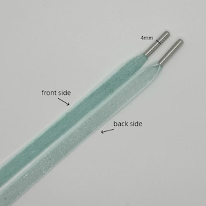 May include: A pair of light blue shoelaces with silver aglets. One side of the shoelace is a solid light blue color, while the other side has a subtle glitter finish. The shoelaces are 4mm wide.