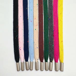 Op de afbeelding: Een verzameling kleurrijke veters met metalen veteroogjes. De veters zijn in verschillende kleuren, waaronder zwart, roze, marineblauw, lichtblauw, beige, bruin, groen, grijs, felroze en geel. Elke veter heeft een gespikkeld patroon.
