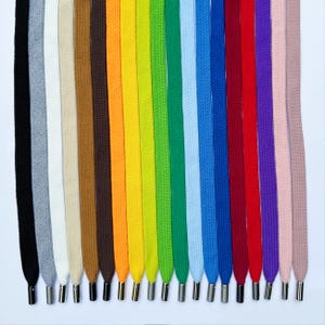 Pode incluir: Uma coleção de 18 cadarços em várias cores, incluindo preto, branco, cinza, marrom, laranja, amarelo, verde, azul, vermelho, roxo e rosa. Os cadarços são todos do mesmo comprimento e têm pontas metálicas prateadas.