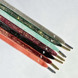 May include: Seven different colors of glitter ribbon, each with a number label. The ribbons are arranged in a fan shape, with the lightest color at the top and the darkest color at the bottom. The colors are: silver, light green, light blue, burgundy, dark green, black, and coral.