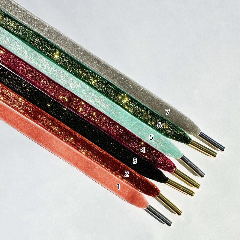 May include: Seven different colors of glitter ribbon, each with a number label. The ribbons are arranged in a fan shape, with the lightest color at the top and the darkest color at the bottom. The colors are: silver, light green, light blue, burgundy, dark green, black, and coral.