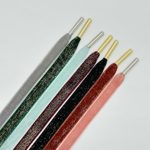 May include: A set of six shoelaces in various colors, including gray, green, mint, burgundy, black, and orange. Each shoelace has a gold-colored metal tip and a silver-colored metal aglet.