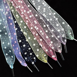 May include: A selection of star-patterned shoelaces in a range of colours. The sheer laces feature white stars and silver metal aglets. Colours include blue, purple, pink, and green. The laces are ideal for adding a touch of flair to footwear.