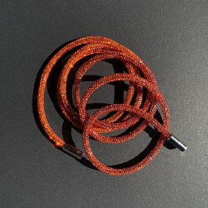 Puede incluir: Un brazalete de cristal naranja enrollado con un cierre plateado. El brazalete está hecho de pequeños cristales brillantes.