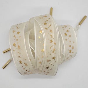 May include: White satin ribbon with gold star print. The ribbon is rolled up and has gold metal tips.