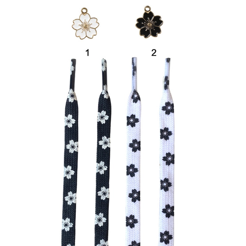 May include: Two pairs of shoelaces with a black and white floral pattern. The shoelaces are shown with two different charms, one with a white flower and one with a black flower.