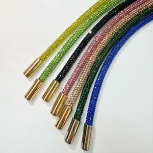 May include: A set of six colorful rhinestone chains with gold-toned end caps. The chains are made of small, sparkling rhinestones in shades of green, black, pink, gold, blue, and dark blue.