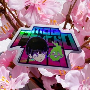 Puede incluir: Pegatina holográfica con personajes de la serie de anime Mob Psycho 100. La pegatina tiene forma rectangular con borde blanco e incluye el logo del programa e ilustraciones de personajes. El fondo es un arreglo floral rosa suave.