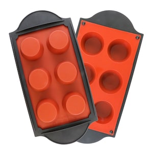 May include: Two silicone baking molds with a black rim. The mold on the left has six round cavities, while the mold on the right has five round cavities. Both molds are red.