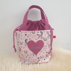 Puede incluir: Bolsa de cord&oacute;n rosa con un coraz&oacute;n rosa que dice "Lana". La bolsa tiene un estampado de unicornios rosa y blanco con castillos y corazones.