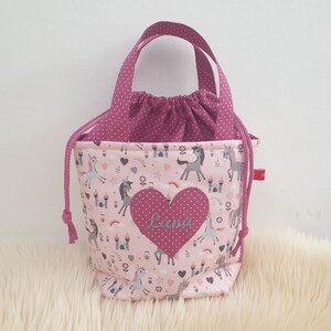 Puede incluir: Bolsa de cord&oacute;n rosa con estampado de unicornio y castillo. La bolsa tiene un coraz&oacute;n rosa con el nombre "Lana" bordado.