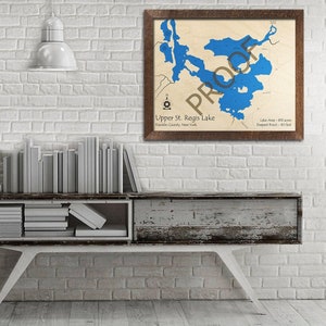 May include: A framed map of Upper St. Regis Lake in Franklin County, New York. The lake is shown in blue, with surrounding land in beige. The map includes the lake's area and deepest point.
