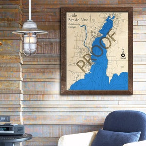 May include: A framed map of Little Bay de Noc in Delta County, Michigan. The map shows the shoreline and depth contours of the bay in blue.