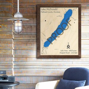 May include: A framed map of Lake McDonald in Flathead County, Montana. The lake is shown in blue, with surrounding land in brown. The map includes the lake's area and deepest point.