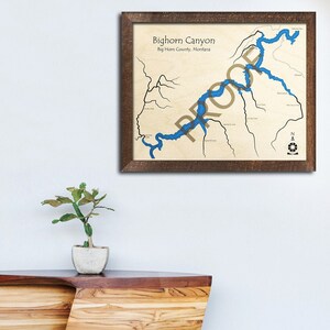 May include: A framed map of Bighorn Canyon, Big Horn County, Montana. The map shows the lake and surrounding area in detail. The map is framed in a dark brown wood frame.