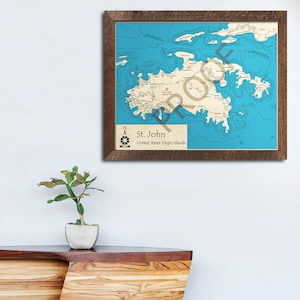May include: A framed nautical map of St. John, United States Virgin Islands, with a blue background and brown lines depicting the coastline and waterways. The map is framed in a dark brown wood frame.