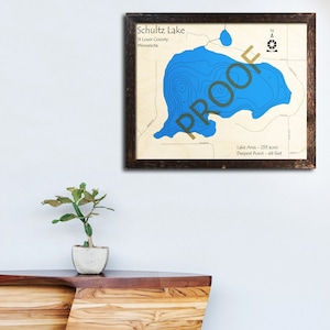 May include: A framed map of Schultz Lake in St. Louis County, Minnesota. The map shows the lake's depth contours in blue, with a compass rose and the text "Lake Area - 255 acres, Deepest Point - 48 feet".