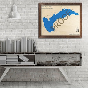 May include: A framed map of Ashley Lake in Flathead County, Montana. The map shows the lake's outline and depth contours in blue. The text "PROOF" is printed over the map in white. The map also includes the lake's area and deepest point.