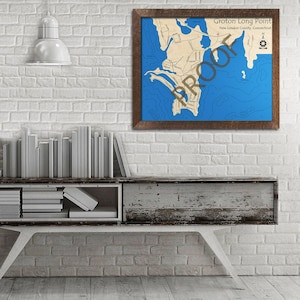 May include: A framed nautical map of Groton Long Point, New London County, Connecticut. The map is printed on a cream-colored background with blue water features. The frame is brown wood.