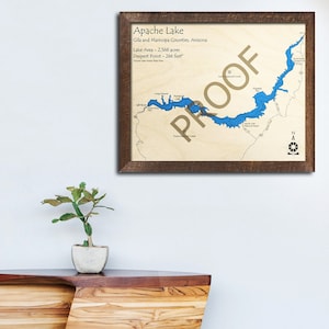 May include: A framed map of Apache Lake in Arizona, showing the lake's outline in blue, with surrounding land features and text labels. The text reads "Apache Lake", "Gila and Maricopa Counties, Arizona", "Lake Area - 2,568 acres", "Deepest Point - 266 feet", and "PROOF" in a large, stylized font.