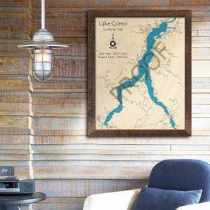 May include: A framed map of Lake Como in Italy, with a blue outline of the lake and surrounding land features. The map includes the text "Lake Como", "Lombardy, Italy", "Lake Area - 36,077 acres", and "Deepest Point - 1,345 feet".