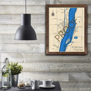 May include: A framed map of the St. Clair River, showing the river's course through Marine City, Michigan and Sarnia, Ontario. The map is printed on a beige background with blue water and black lines for roads and other features.