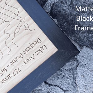 May include: A wooden map of a lake with a black matte frame. The map shows the lake's area, deepest point, and the depth in feet. The text on the map reads "Lake Area - 79.7 acres, Deepest Point - 185 feet".